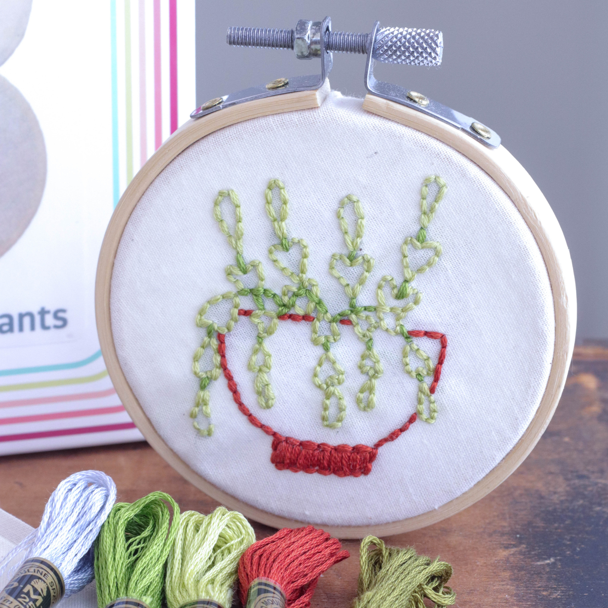 Embroidery hoop with embroidered plants design on a wooden surface with embroidery threads.
