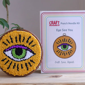 Punch needle art with eye design next to a Craft Habit kit packaging.