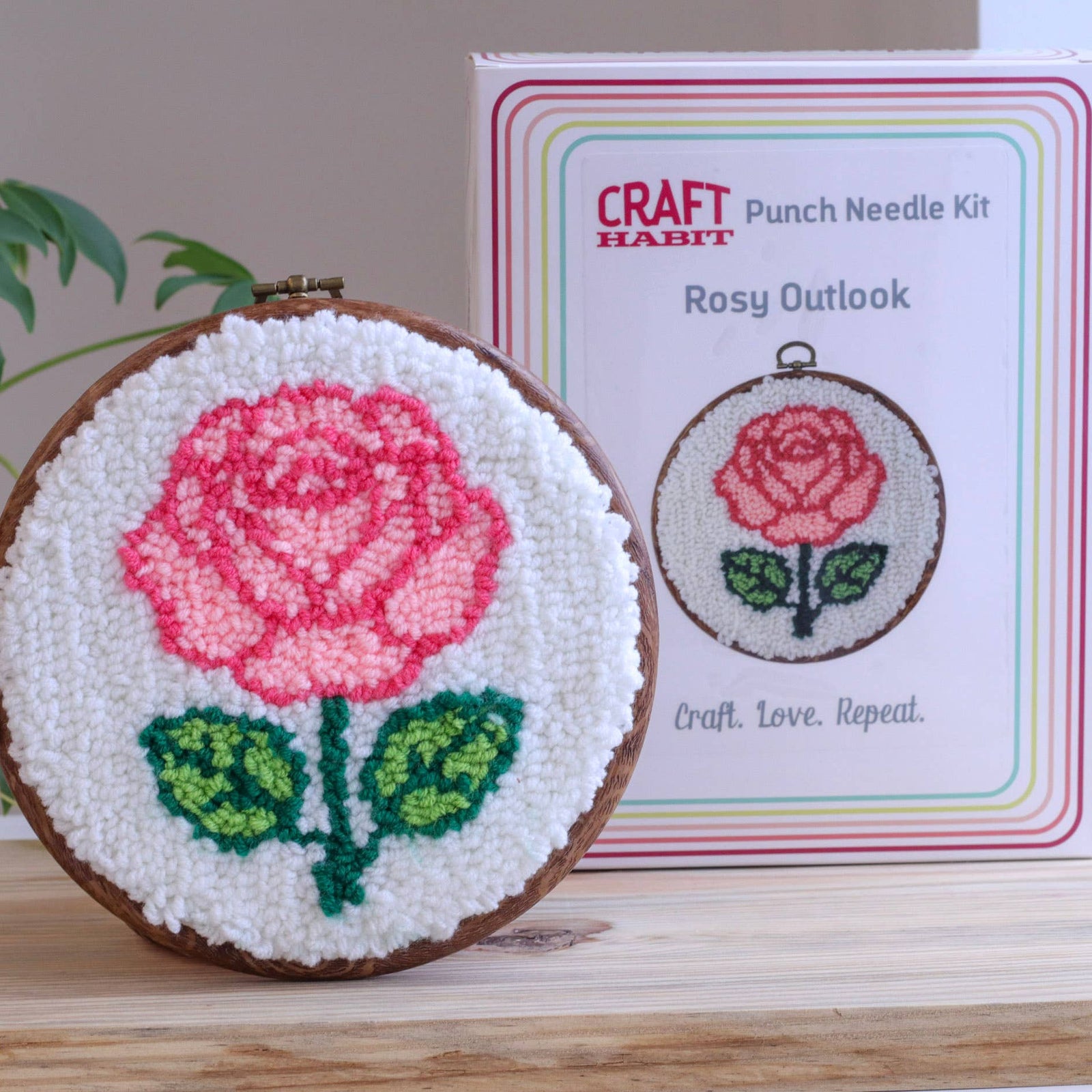 Punch needle art with a pink rose and green leaves, displayed in front of a 'Craft Habit' kit box.