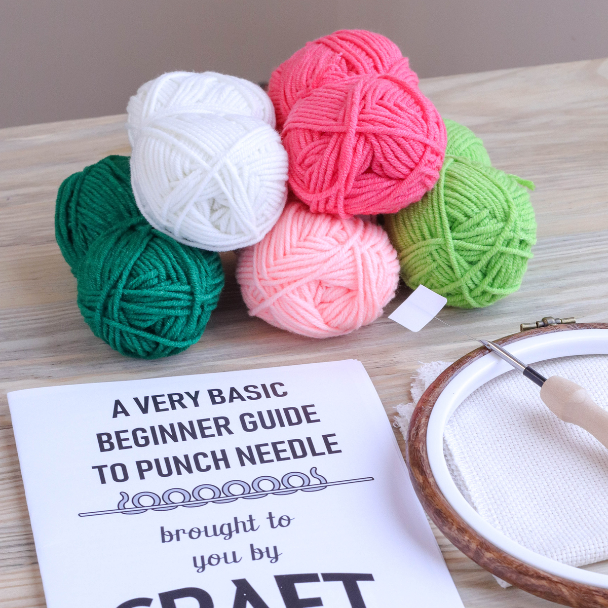 Colorful yarn balls with a book titled 'A Very Basic Beginner Guide to Punch Needle' on a wooden surface.