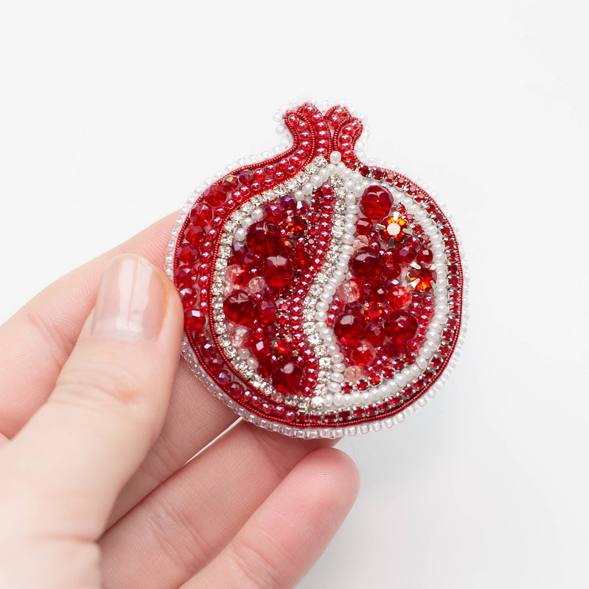 Hand holding a red and white beaded pomegranate ornament against a white background