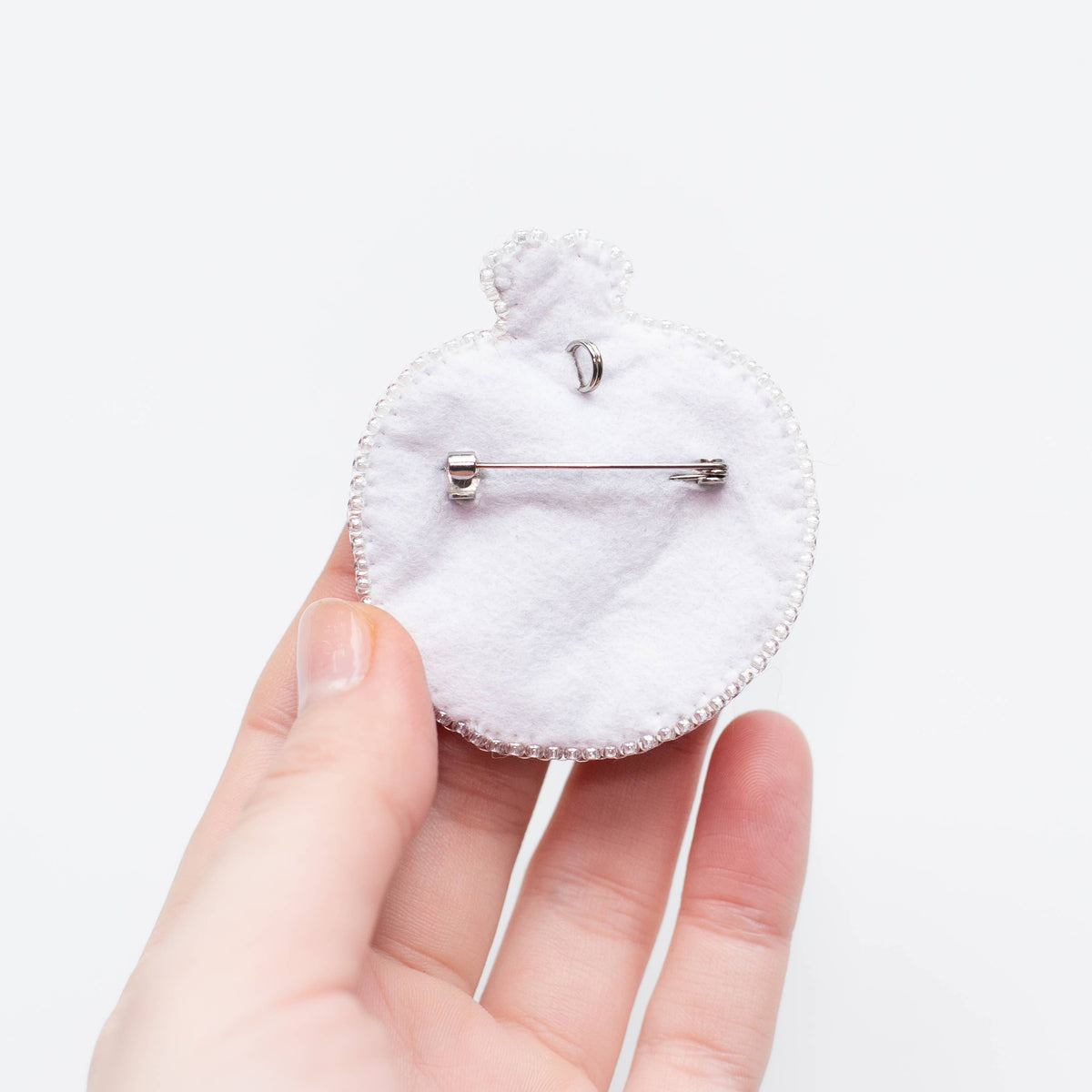 White circular brooch back held by a hand on a white background