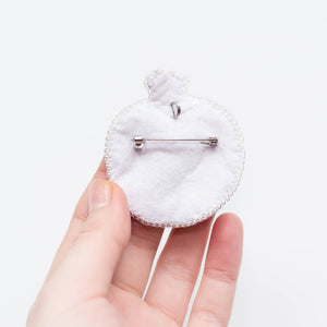 White circular brooch back held by a hand on a white background
