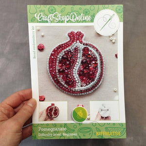 Packaged craft kit with pomegranate design held by a hand on a gray background