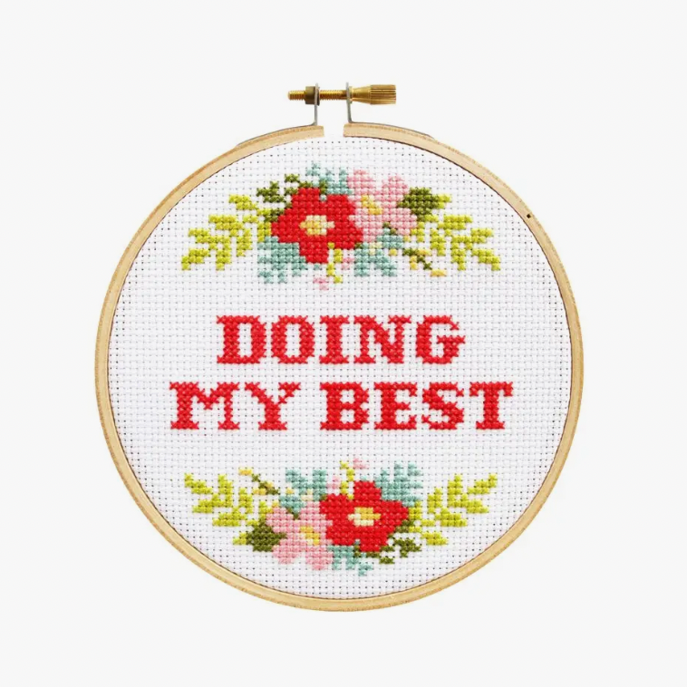 A cross stitch kit with the phrase 'DOING MY BEST' surrounded by a floral pattern, displayed in an embroidery hoop.