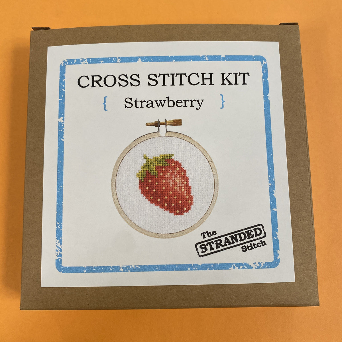 Cross stitch kit with strawberry design and box with 'The Stranded Stitch' branding on a white background