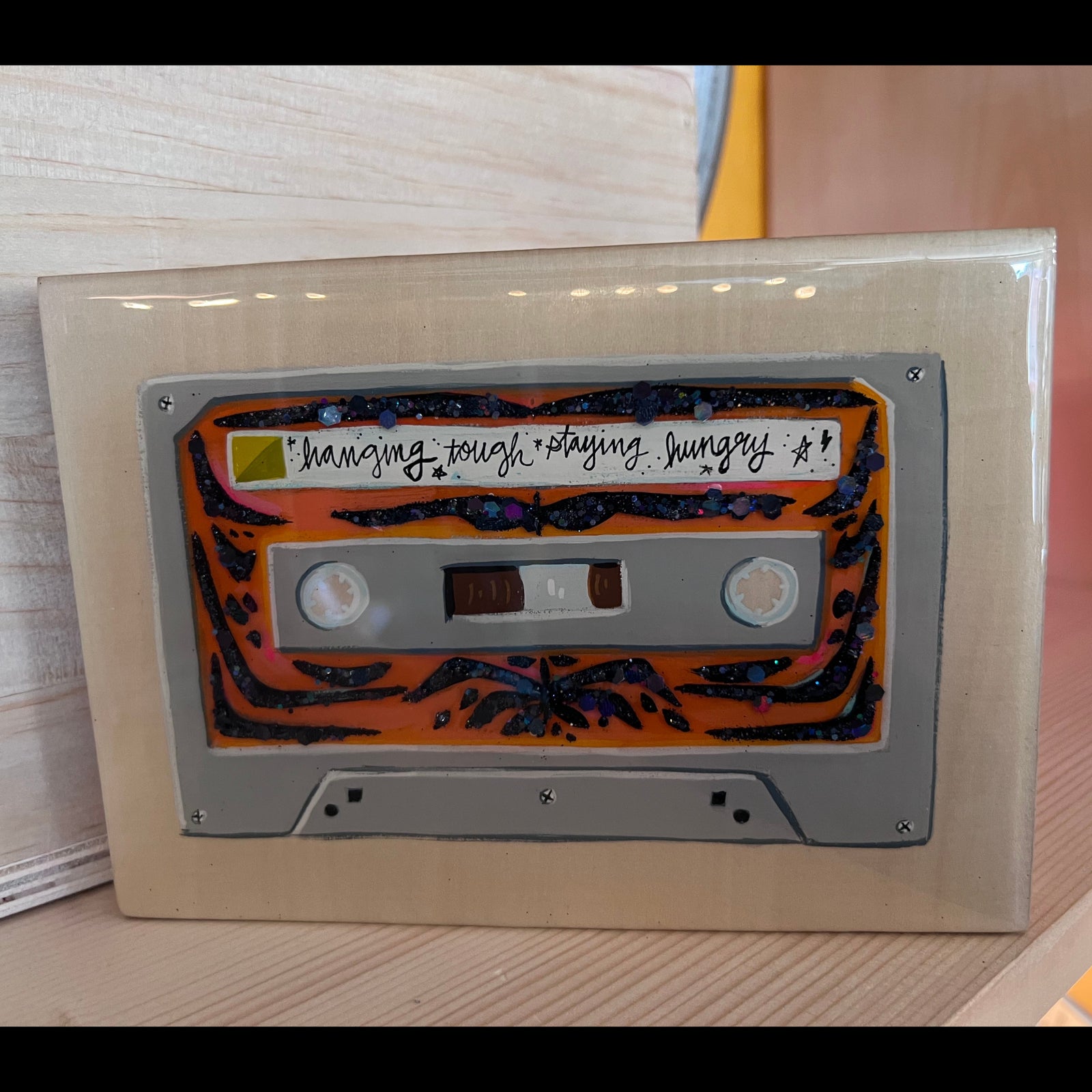 Painting of a cassette tape with a tiger stripe pattern that says "hanging tough staying hungry" on the label. 