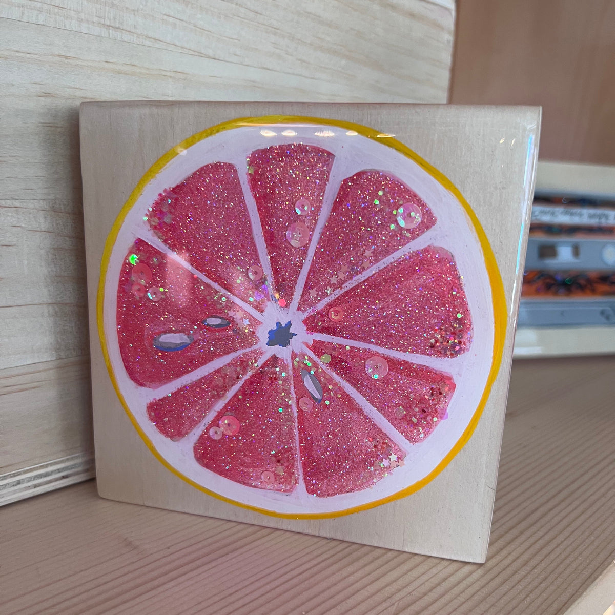 A small painting of a sparkly pink grapefruit. 
