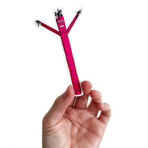 Hand holding a sticker of a pink air dancer in cartoon form. 