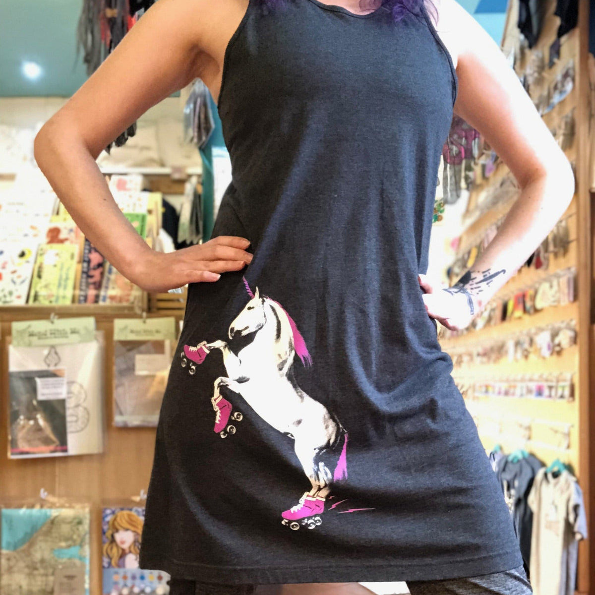 Person wearing a black sleeveless dress with a roller skating unicorn design in a store setting. 