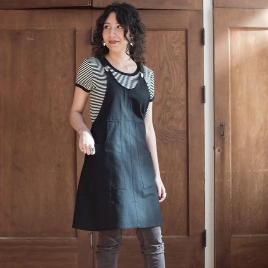Woman wearing a black apron over a striped shirt in a room with wooden walls.