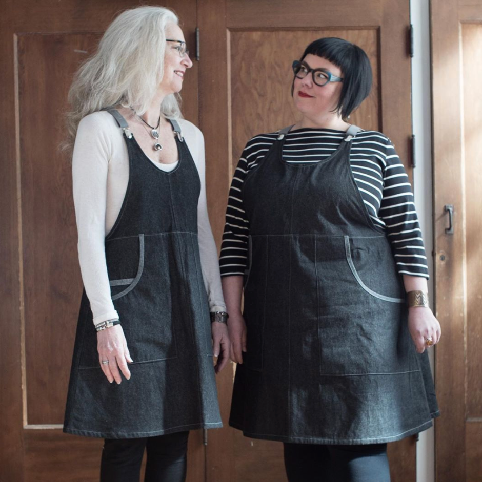 Two women wearing black apron dresses standing in a room with wooden doors.