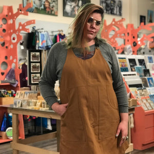 Woman wearing a brown apron dress in a store setting with colorful decorations and products.