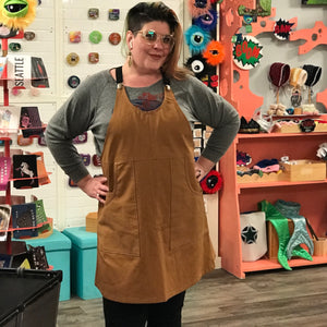 Woman wearing a brown apron dress in a store with colorful decorations.