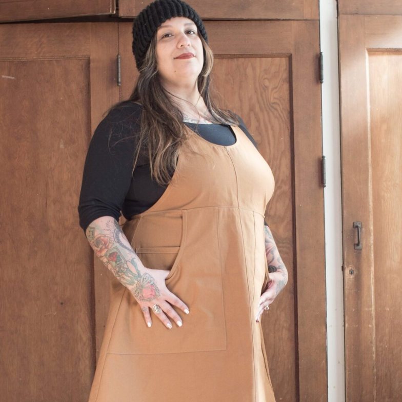 Person wearing a tan apron dress standing in front of wooden doors.