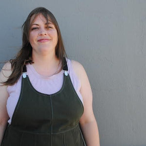 Woman wearing a green apron over a pink shirt against a gray wall