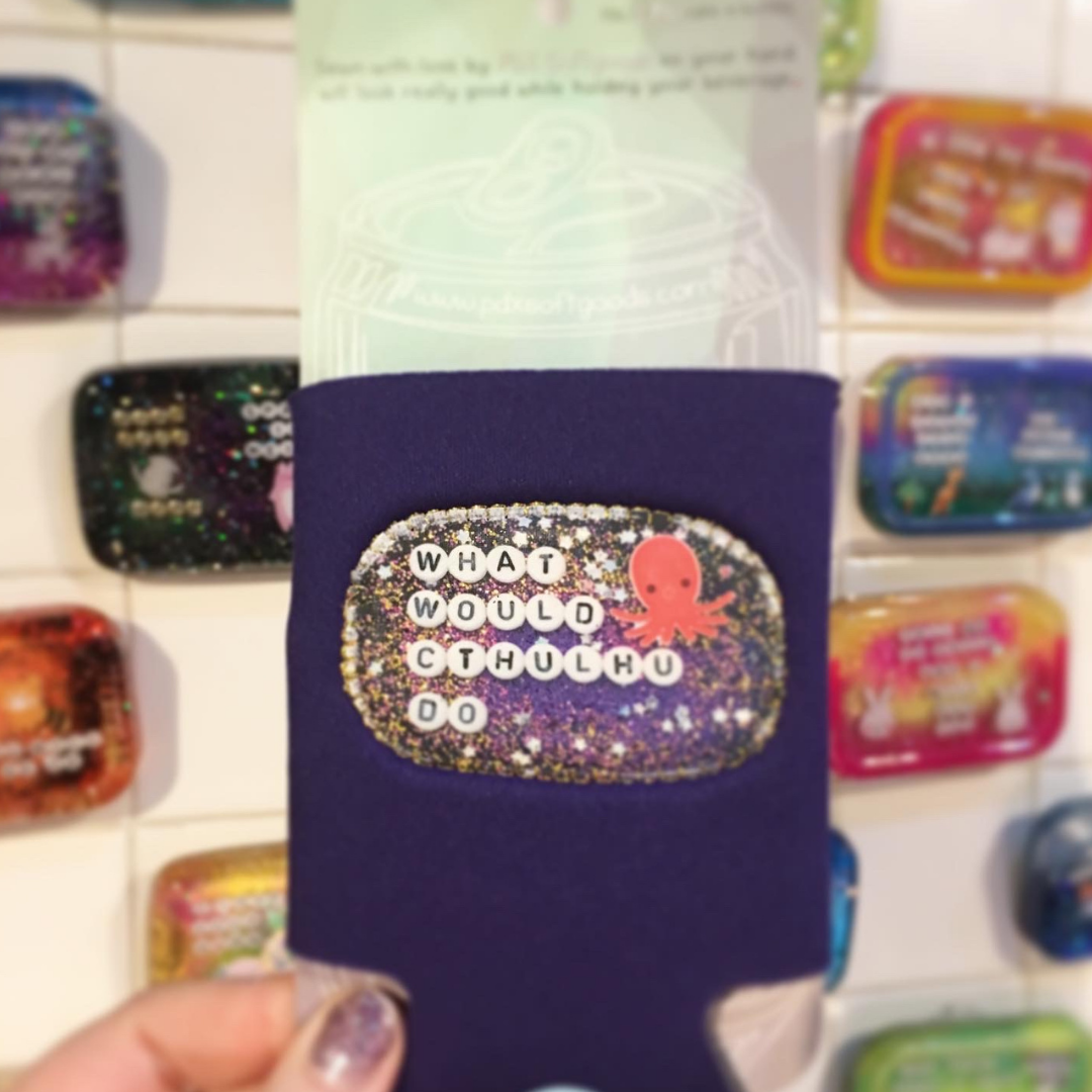 A purple can cooler with a patch on the front that says "What would Cthulhu do?"