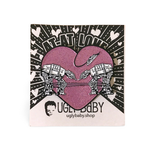 Heart shaped enamel pin called Love AT-AT First Sight with a pink glitter background. Shown on a backing card with hearts. 