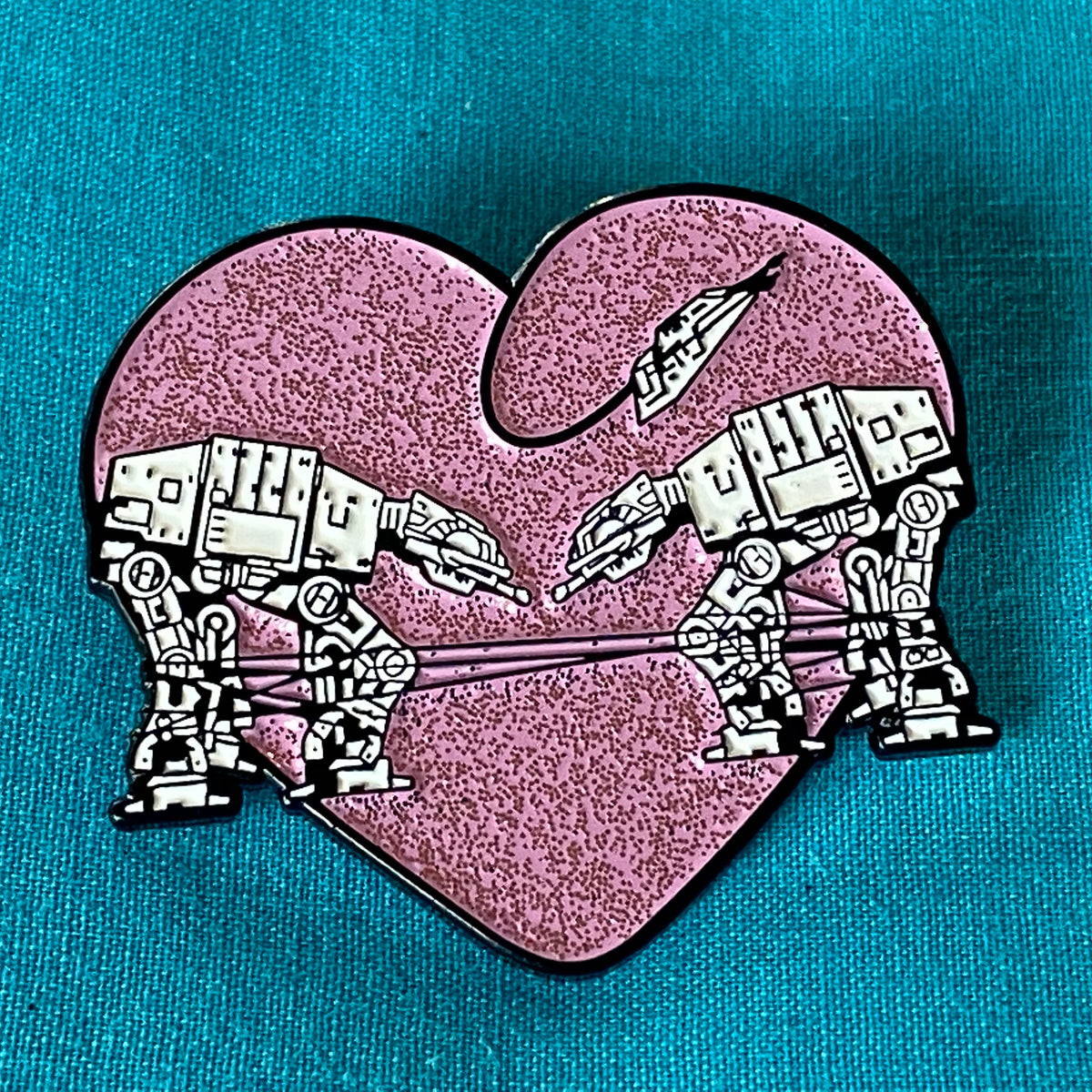 Heart shaped enamel pin called Love AT-AT First Sight with a pink glitter background. 