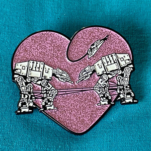 Heart shaped enamel pin called Love AT-AT First Sight with a pink glitter background. 