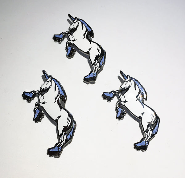 Three identical enamel pins of a rearing white unicorn with a blue mane, tail, and hooves, outlined in black, arranged on a plain white background.