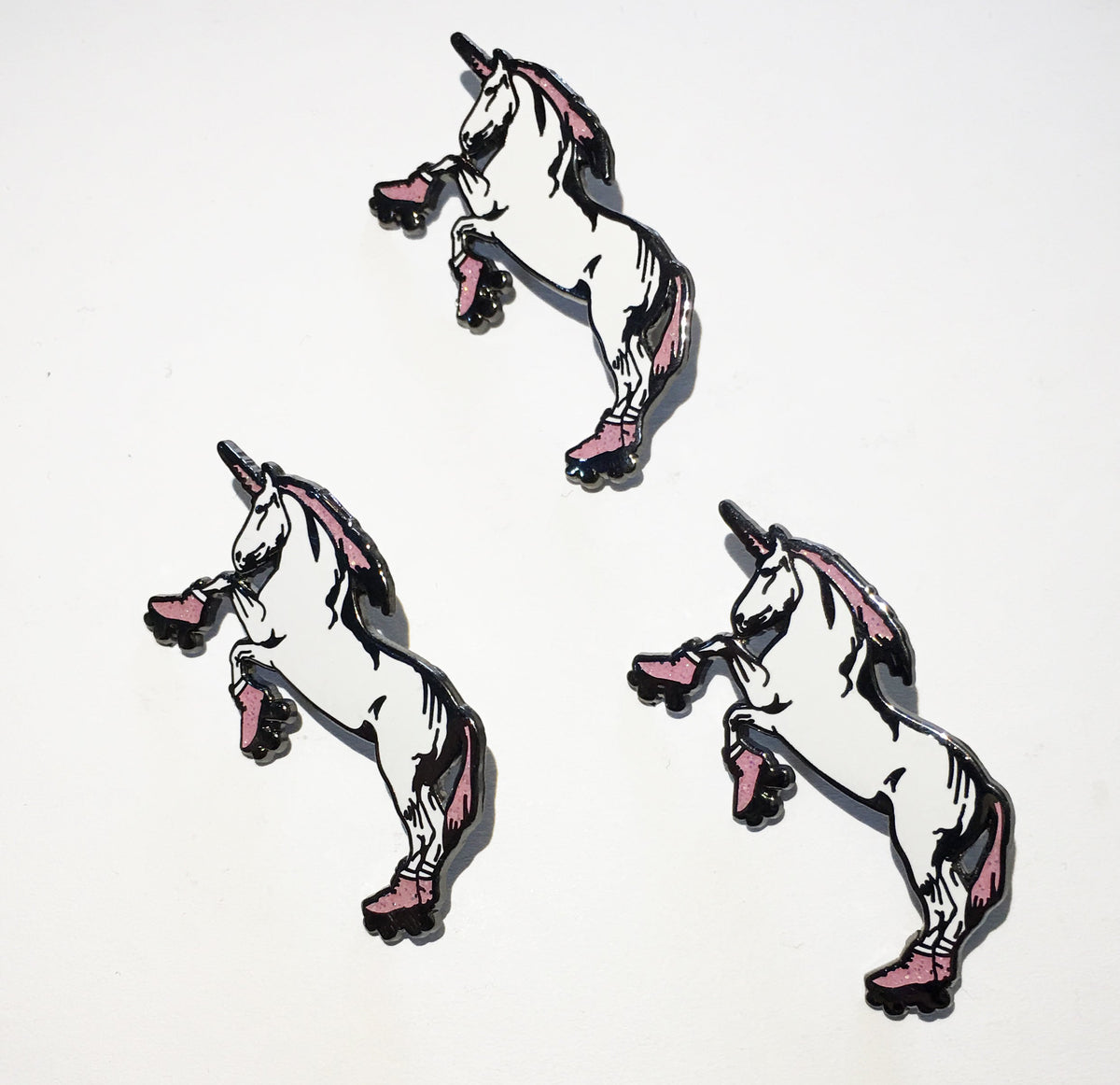Three idential Ienamel pins of unicorns standing on their hind legs and wearing roller skates. 