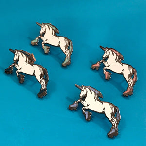 Four small unicorn-shaped accessories arranged on a bright blue background. They are enamel pins with a white body, dark gray to black mane/hooves, and small pink, purple, and blue shading accents.