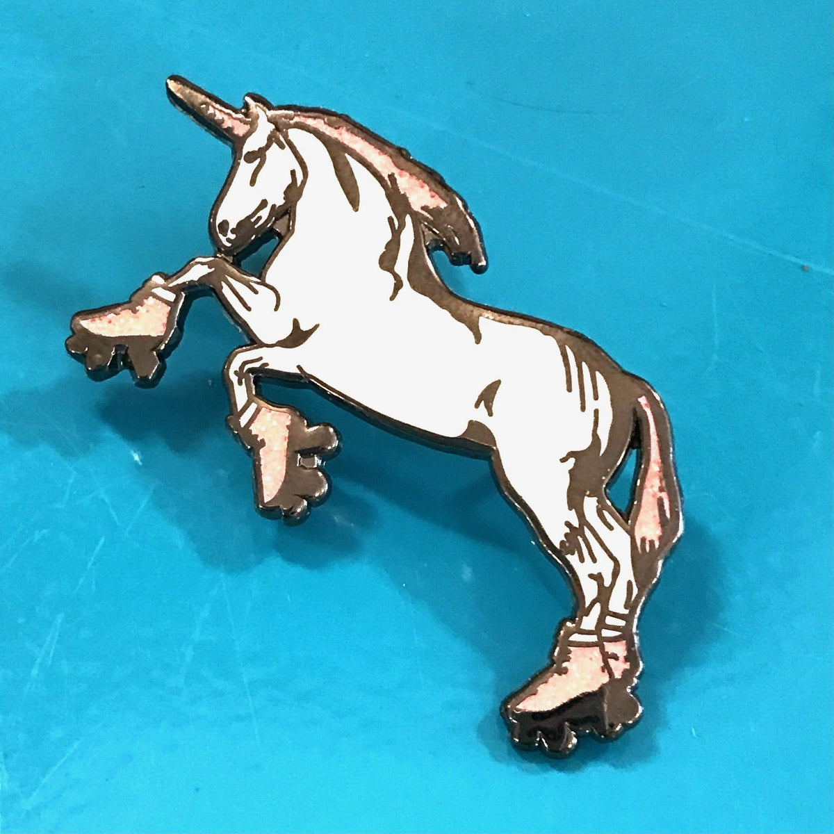 An enamel pin of a unicorn standing on hind legs and wearing roller skates. 