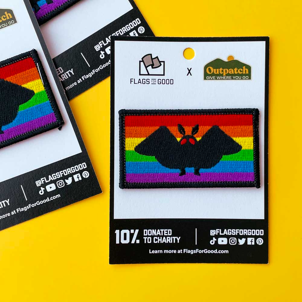An embroidered patch featuring the black silhouette of a moth with legs and red eyes against the rainbow pride flag