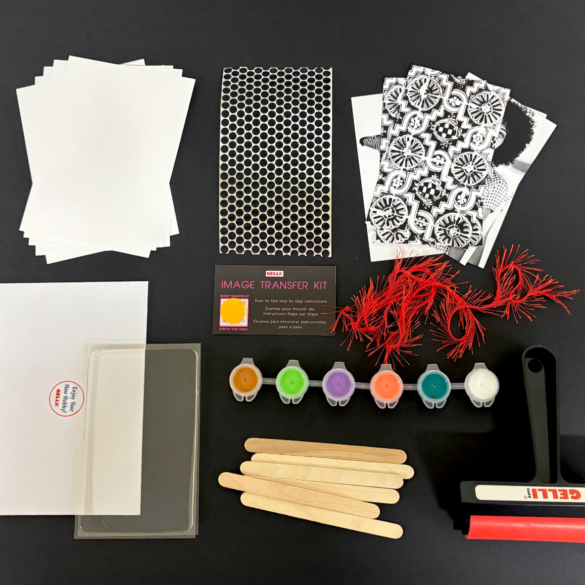Items included in the gelli printing image transfer kit: paper, paint, a brayer, popsicle sticks, images, yarn, punchinella, plate. 