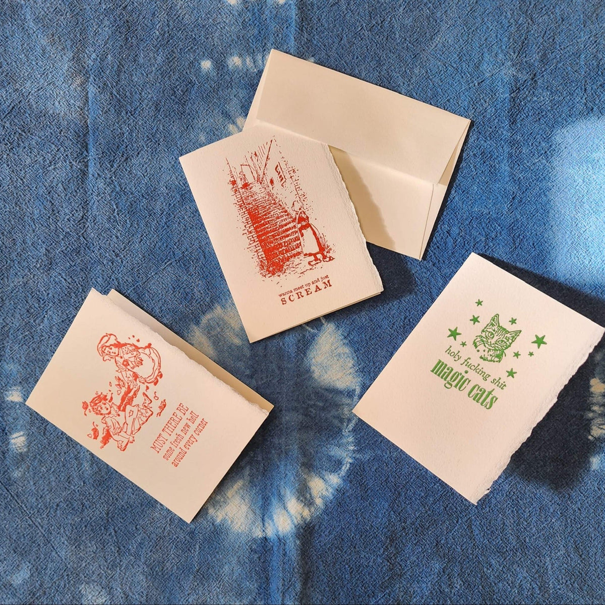 Four letterpress greeting cards with printed designs on a blue textured surface