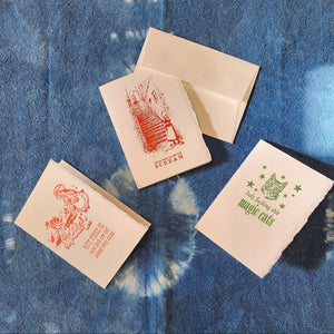 Four letterpress greeting cards with printed designs on a blue textured surface