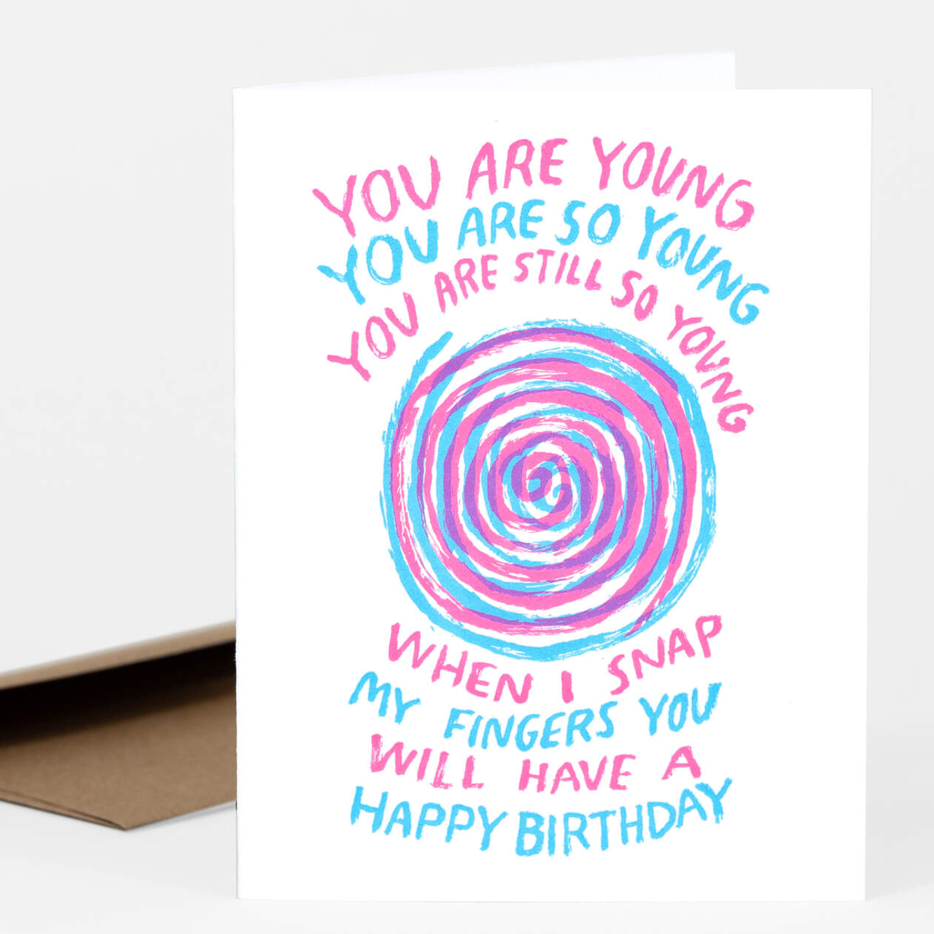 This letterpress greeting card has a bullseye in the middle in pink and blue hypnotic lines. It says "You are young. You are so young. You are still so young. When I snap my fingers you will have a happy birthday." The lettering alternates hot pink and blue. 