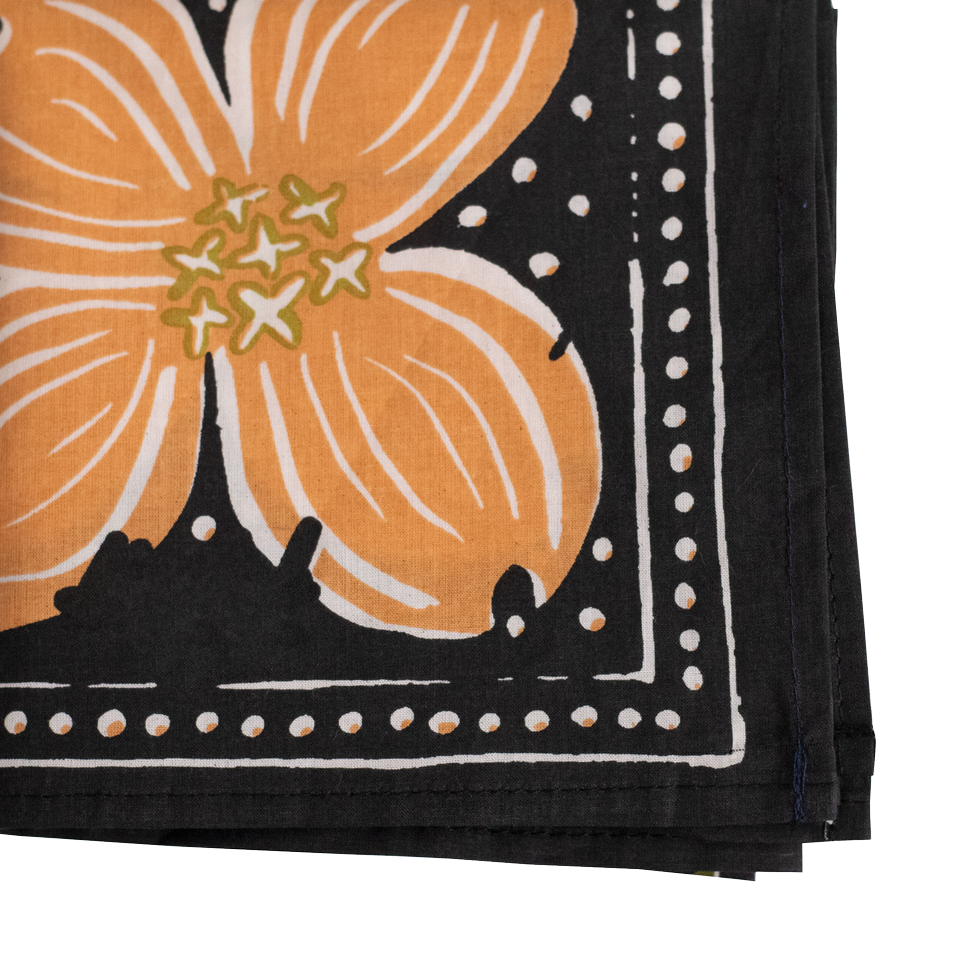 Close-up detail of a bandana corner with a peach colored flower and white dots. 