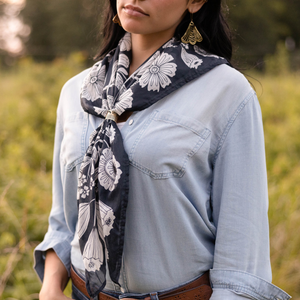 Person wearing a denim shirt modeling a patterned bandana against a blurred natural background. 