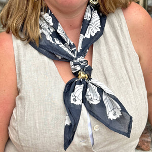 Person modeling a blue and white floral patterned bandana with a gold horse pin. 