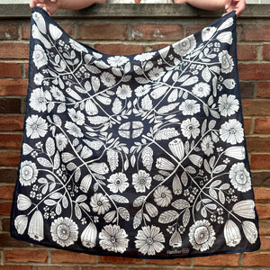 A person holding a blue and white floral patterned bandana against a brick background. 