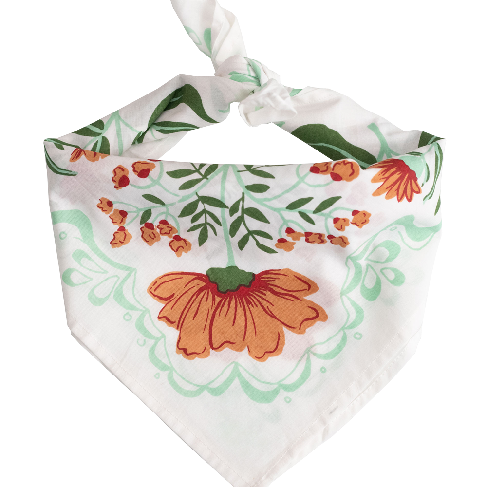 White bandana with a orange and green floral pattern tied into a scarf