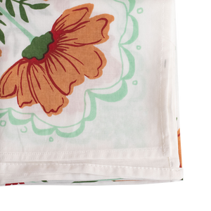 Detail of the corner of a white bandana with an orange and green floral pattern. 