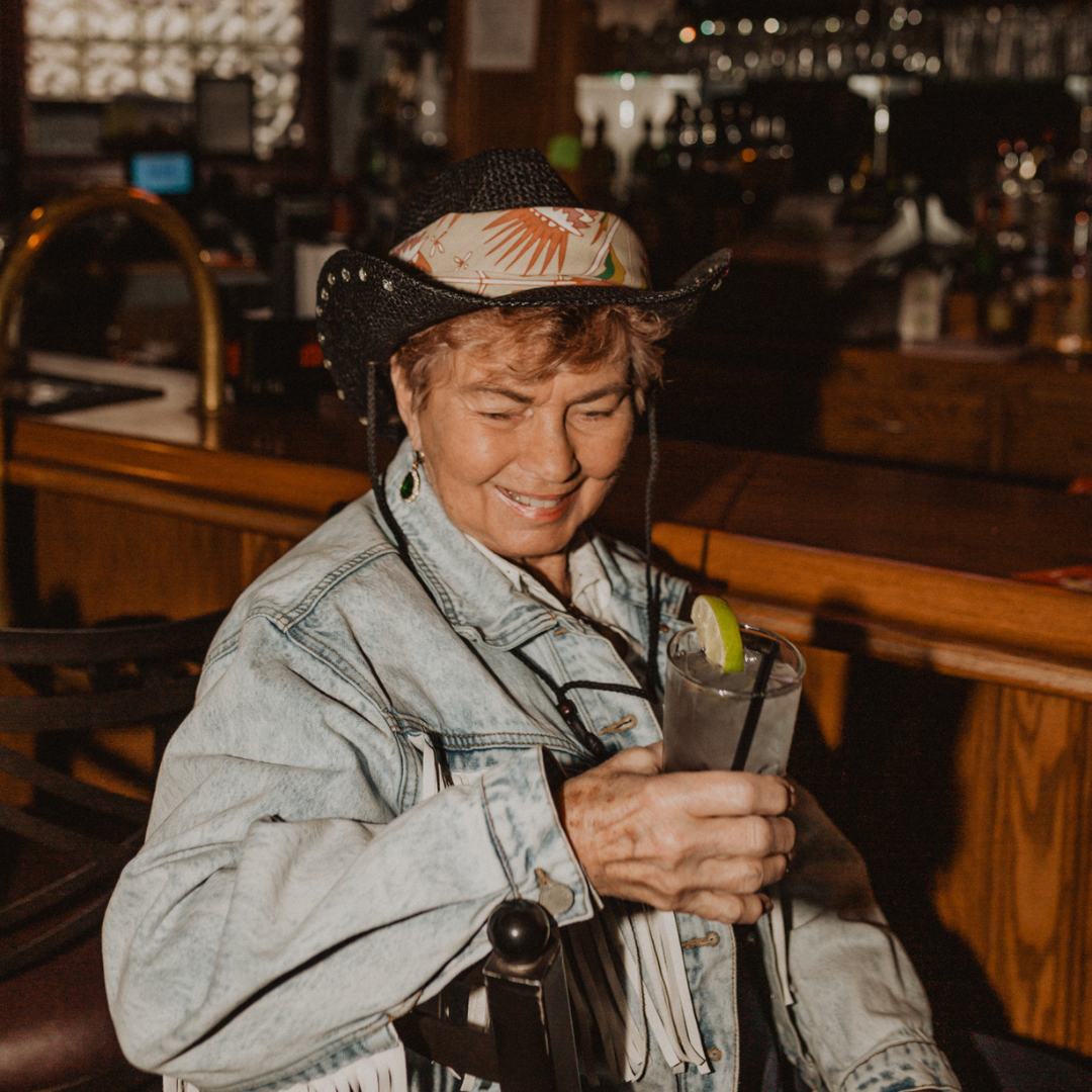 Person wearing a cowboy hat with a floral patterned bandana on it in a bar setting. 