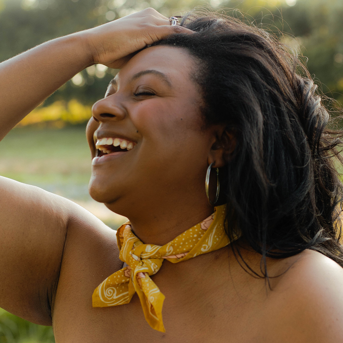  A woman modeling a yellow patterned bandana, wearing it as a scarf around her neck 