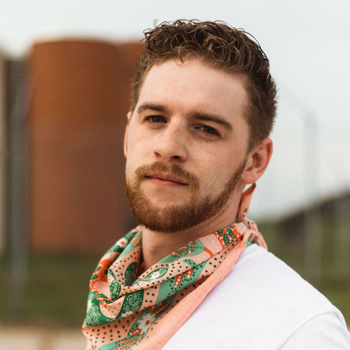 Person wearing a white t-shirt and modeling a pink patterned bandana against a blurred background. 