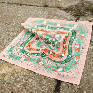 A pink bandana with a snake pattern unfolded on a concrete surface. 