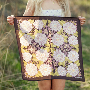 A person holding an unfolded floral patterned bandana in an outdoor setting. 