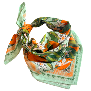 A mint colored bandana with an orange and orange blossom pattern folded and tied into a neck scarf.