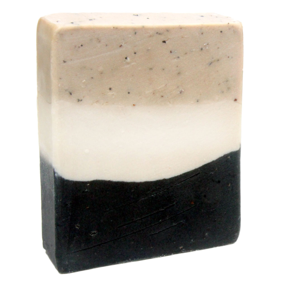 A bar of handmade vanilla chai scented soap with a layer of black color at the bottom, a layer of beige with speckles at the top and the center a solid off-white color. 