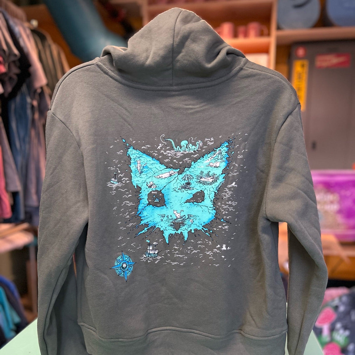Green hoodie with a cat shaped treasure island map on a mannequin in a store setting. 