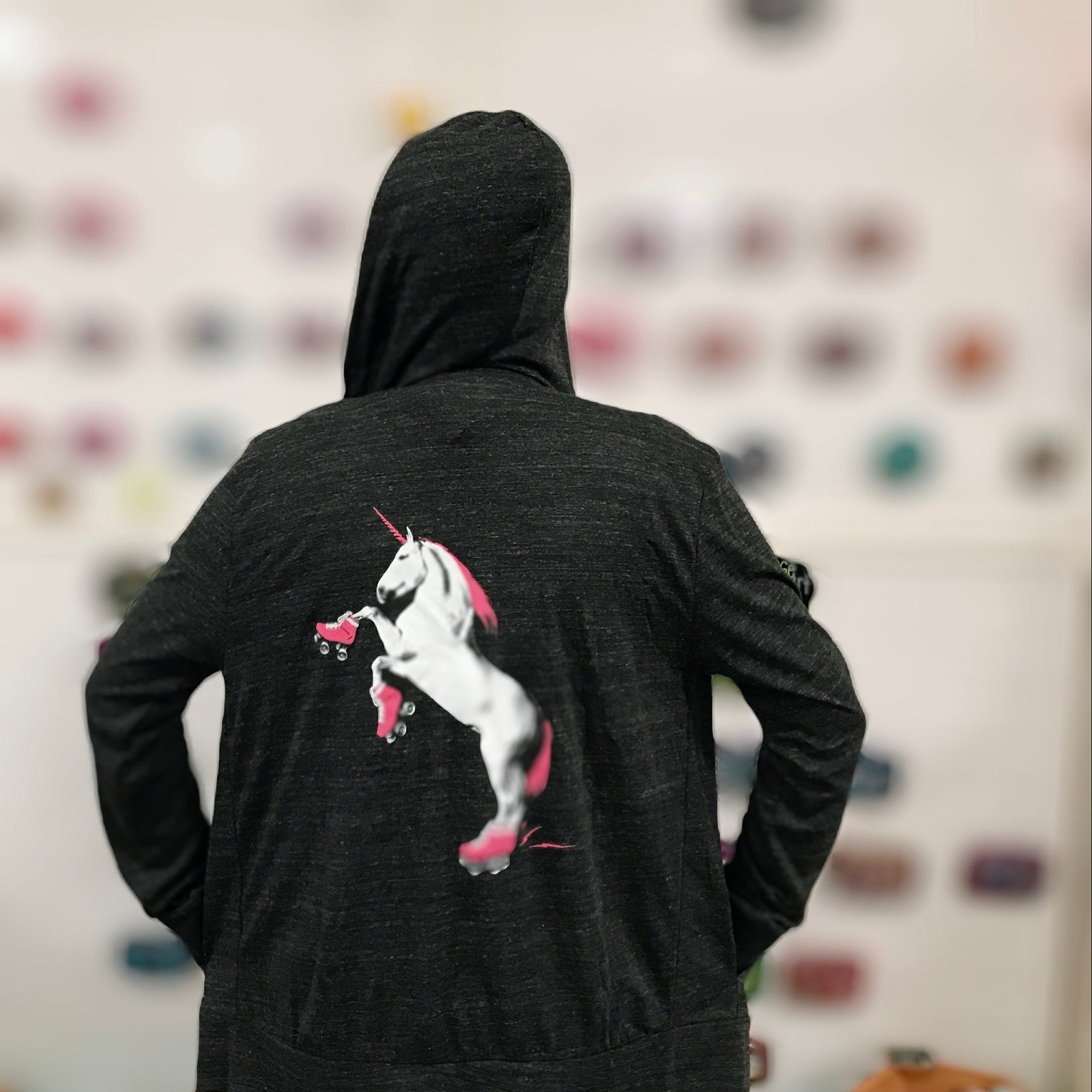 Person wearing a dark hoodie with a unicorn wearing roller skates graphic on the back, against a blurred background.