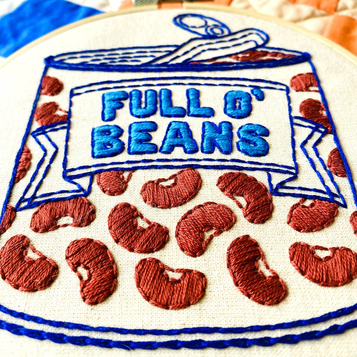 Embroidery hoop with 'Full O' Beans' design on a colorful quilted background