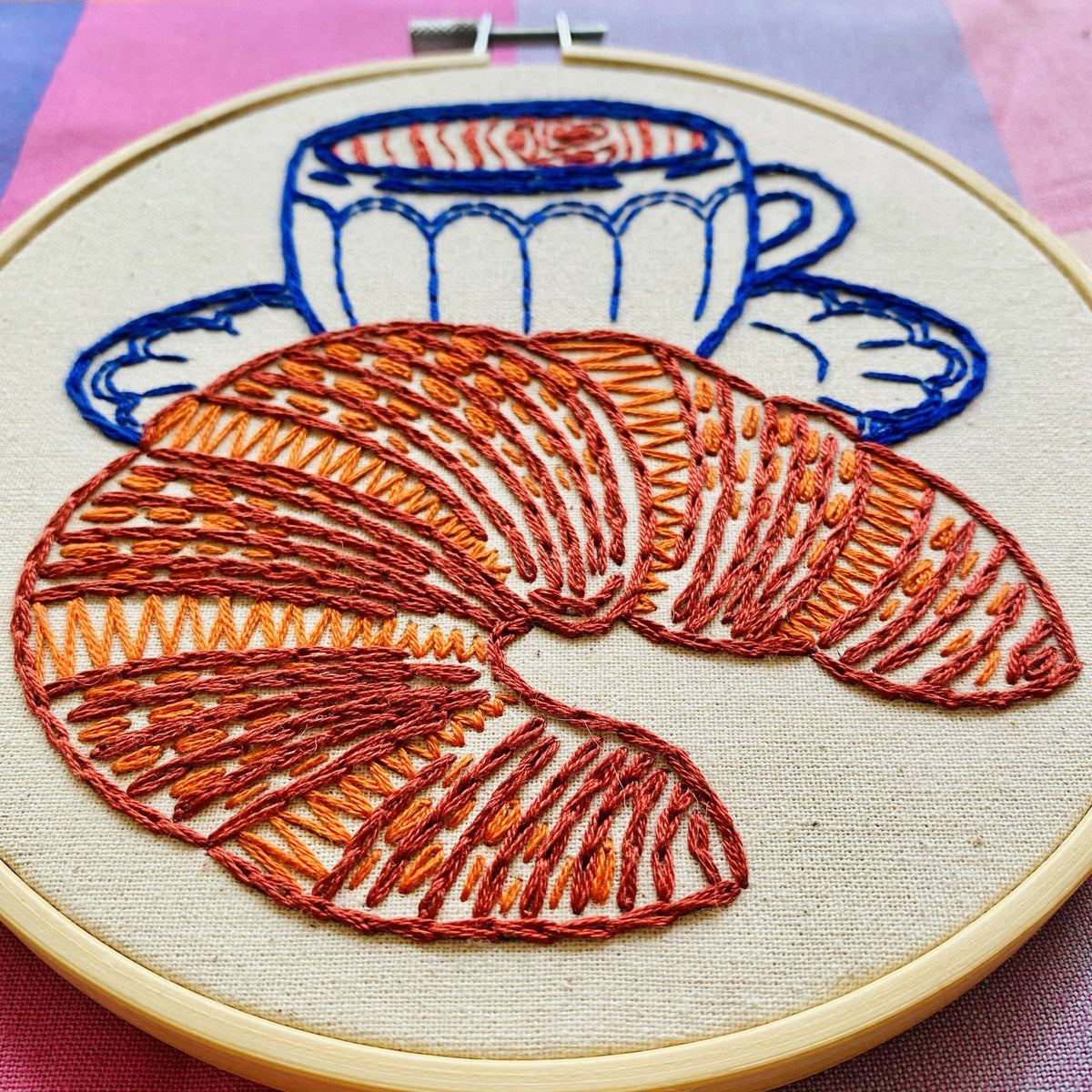 Embroidery hoop with a croissant and coffee cup design on a checkered fabric background